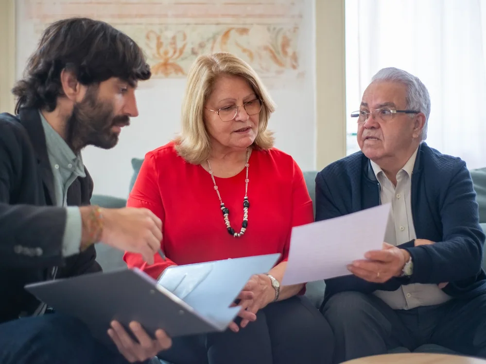 Deux seniors examinent des documents avec une personne qui les accompagne.