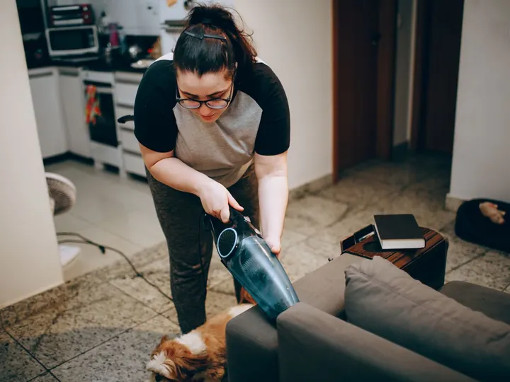 Une femme passe l’aspirateur sur un canapé dans un salon.
